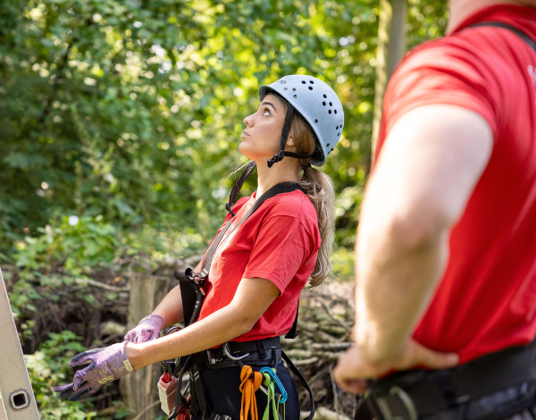 Mitarbeiter bergibt an eine Besucherin die Kletterausrstung